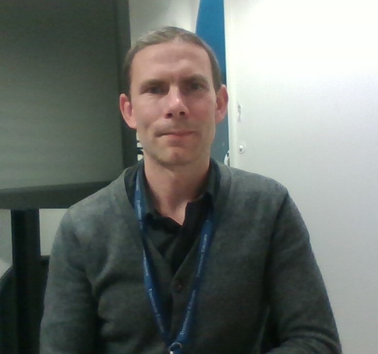 Image of Phil Brunton - a Caucasian male in a grey jumper with a blue lanyard