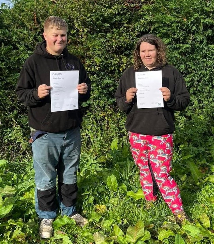 Two young people standing outside holding up their ASDAN certificates