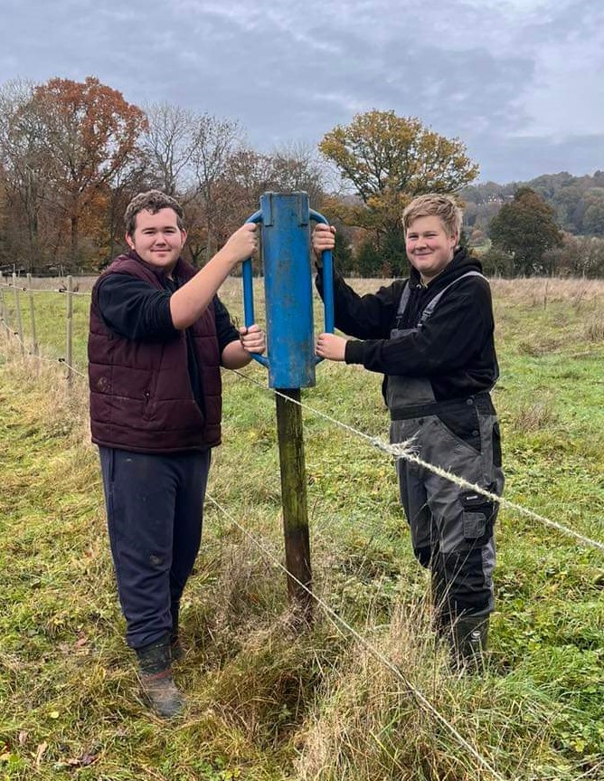 Two young men fixing a post on a farm