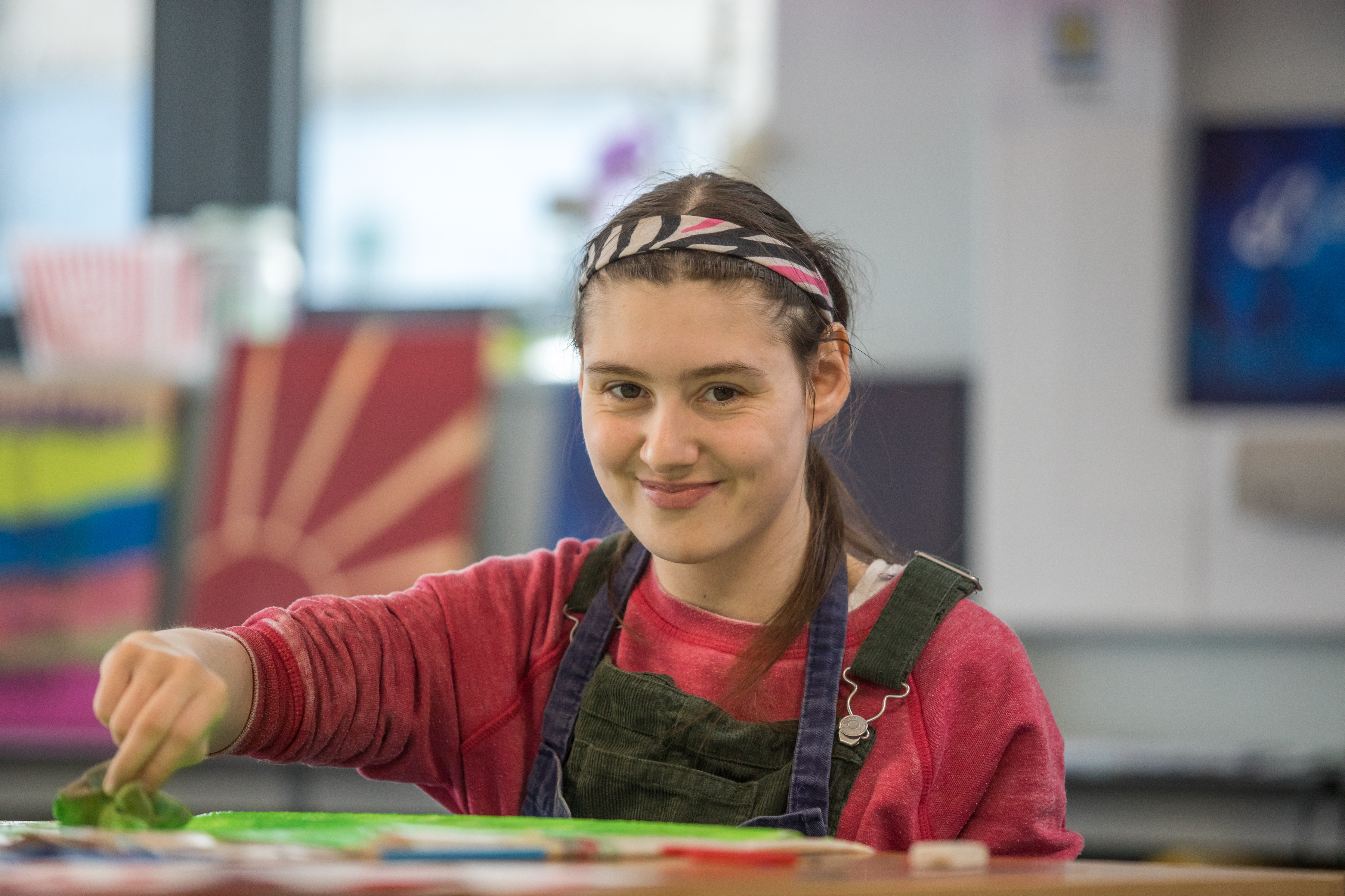 Learner in an apron smiling at the camera as she sponges paint on paper